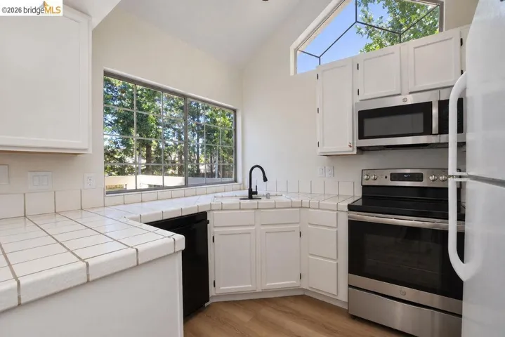 Kitchen with vaulted ceiling, wood-finish flooring, white cabinetry, and stainless steel appliances including a microwave and range