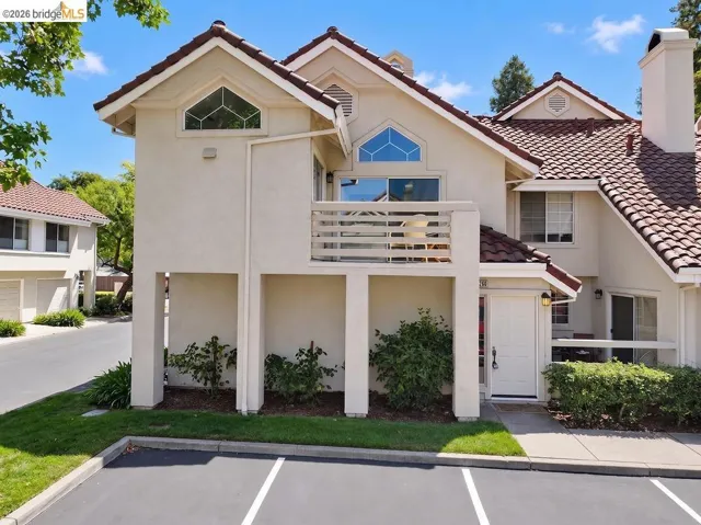 Exterior featuring a tile roof, stucco finish, dedicated parking, upper-level balcony, and a prominent front entry