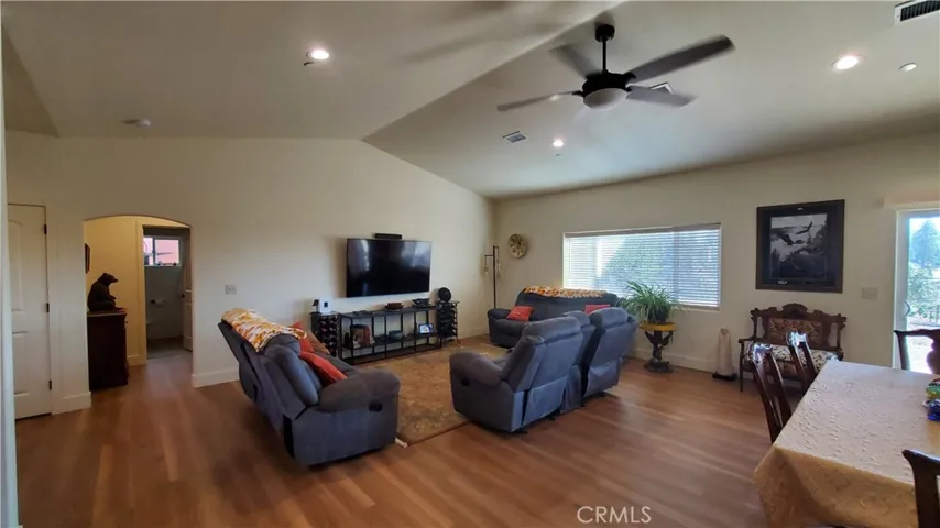 View of living room with vaulted ceilings, window & slider facing back patio area, & arched entry to private guest bedroom & bathroom area.