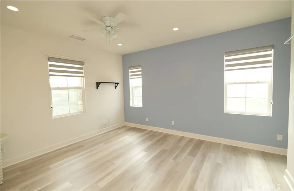 Bright bedroom featuring a blue accent wall, wood-look flooring, and a ceiling fan. Bright bedroom featuring a blue accent wall, wood-look flooring, and a ceiling fan.