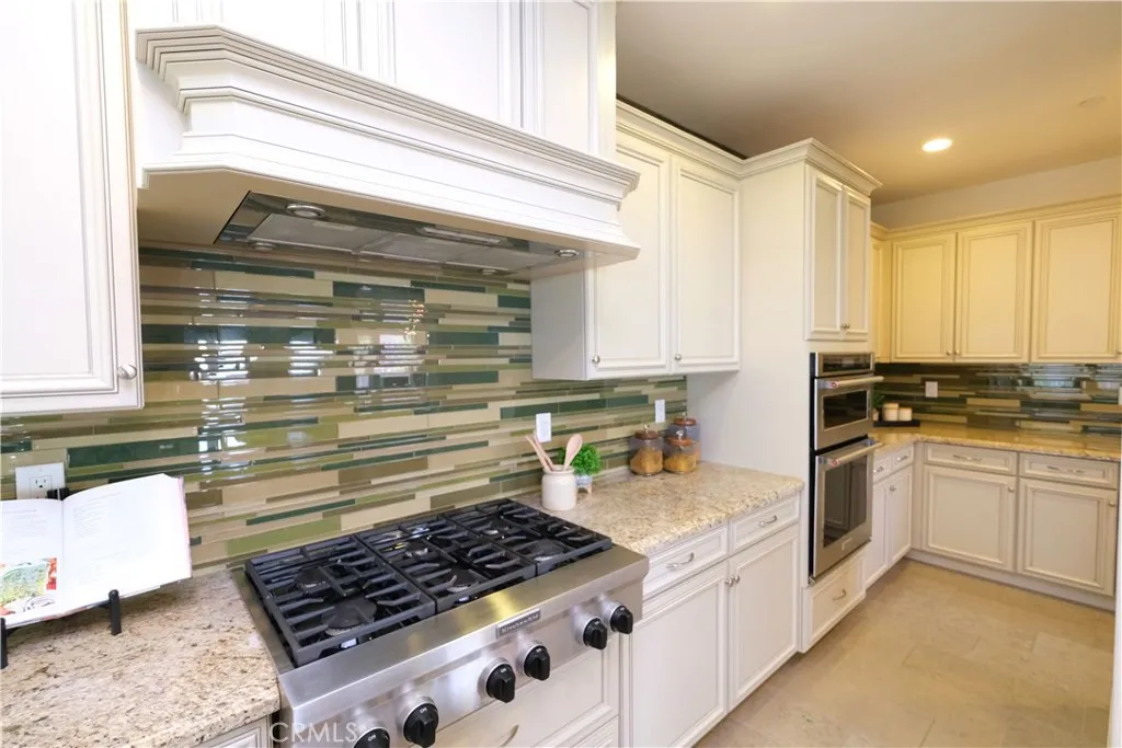 Six-buner gas cooktop beneath a decorative hood surround, complemented by a mosaic backsplash. Six-buner gas cooktop beneath a decorative hood surround, complemented by a mosaic backsplash.