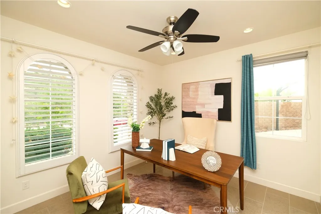 Light-filled home office featuring arched windows, plantation shutters, and a ceiling fan. Light-filled home office featuring arched windows, plantation shutters, and a ceiling fan.