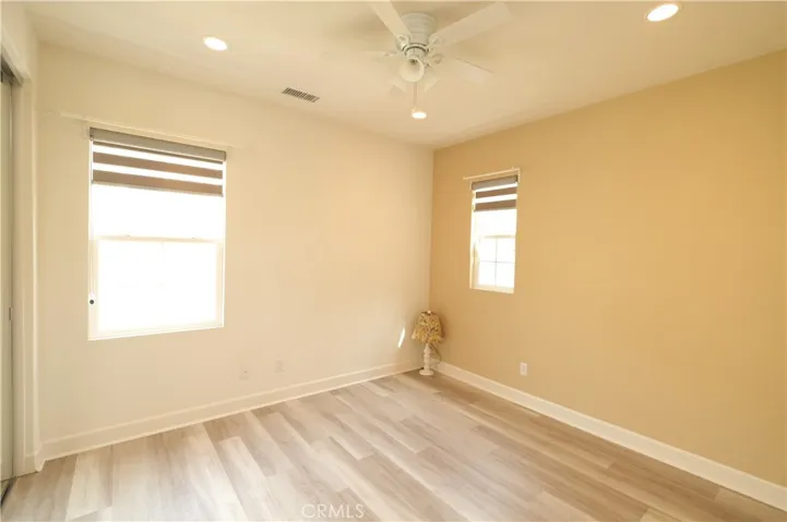 Sunlit bedroom with neutral finishes, woodblock flooring, and windows on two walls.