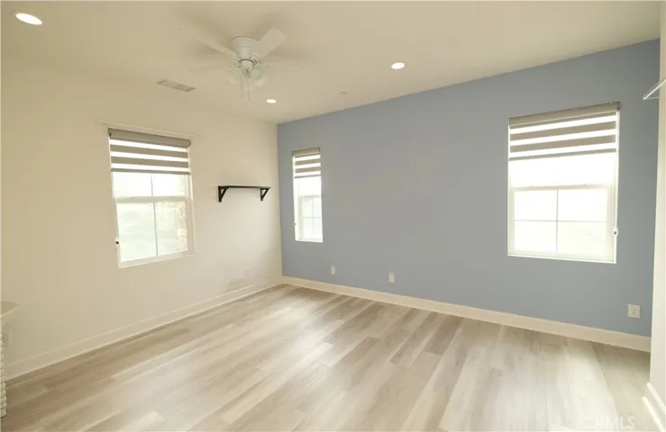 Bright bedroom featuring a blue accent wall, wood-look flooring, and a ceiling fan.