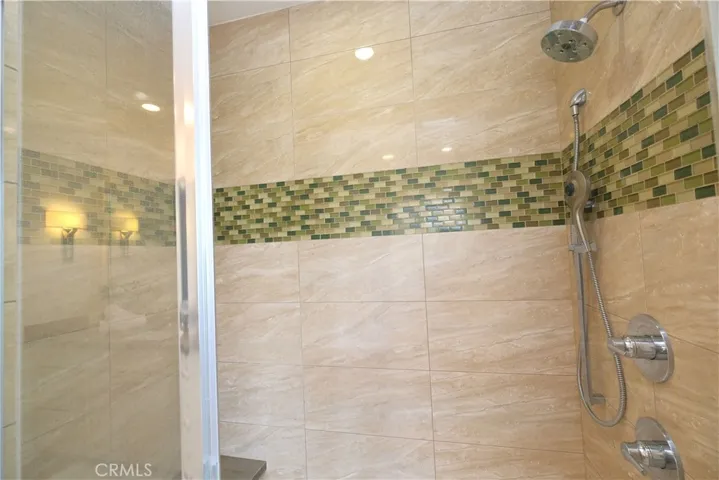 Glass-enclosed showers featuring tiled walls and a decorative mosaic accent band.
