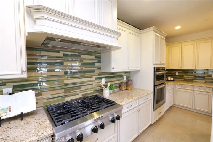 Six-buner gas cooktop beneath a decorative hood surround, complemented by a mosaic backsplash.