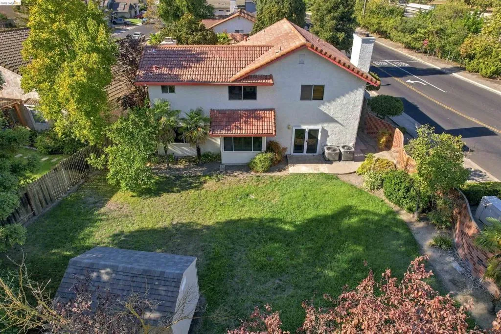 Two-story stucco exterior with a tile roof, featuring a backyard with a grass lawn and a storage shed