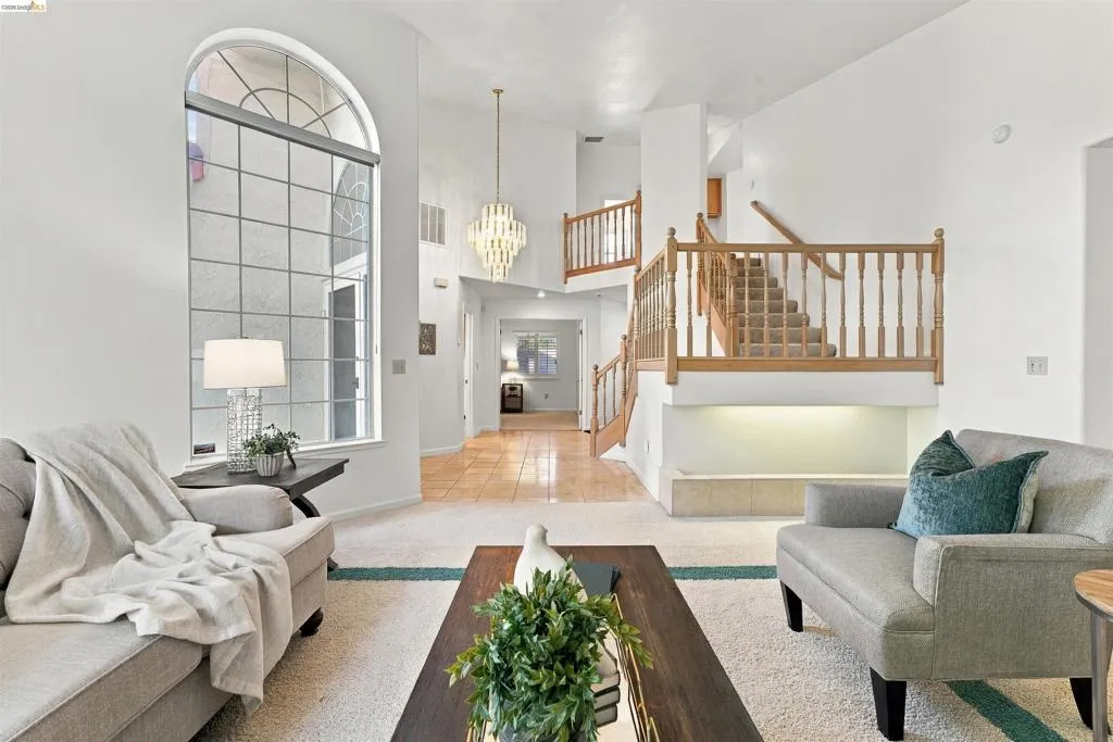 Two-story foyer with an arched, grid-pattern window, wood-finish staircase with balusters, and a tiered chandelier