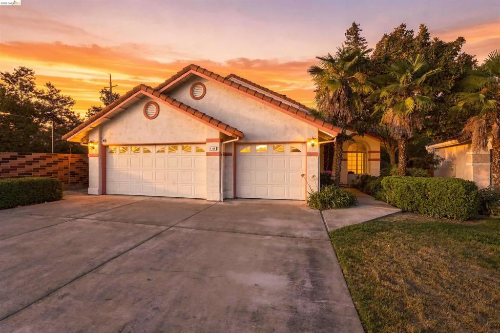 Two-car garage with panel doors, concrete driveway, and stucco exterior with a tile roof