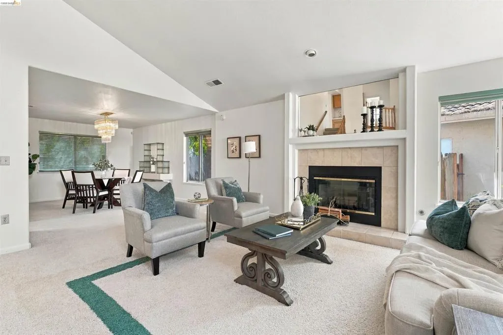 Living area featuring a carpeted floor, tile-surround fireplace, and an open dining area with a tiered chandelier