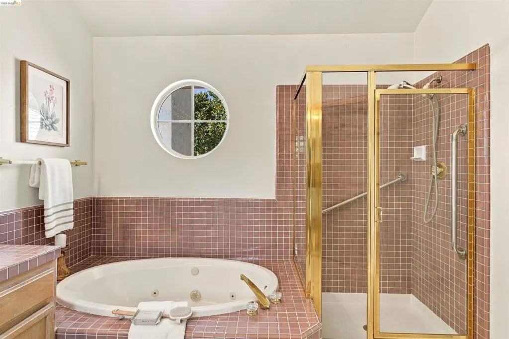 Built-in jetted tub, circular window, and a glass-enclosed shower with gold-tone fixtures