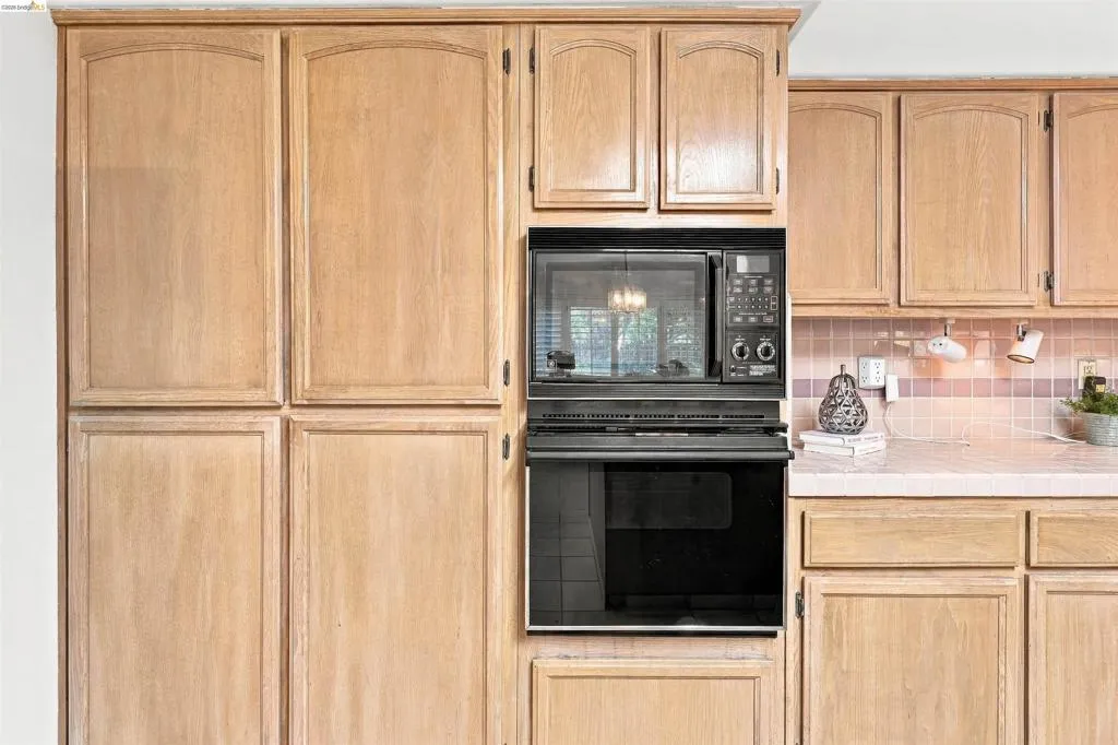 Light wood-finish cabinetry, built-in microwave, wall oven, tile backsplash, and countertop space