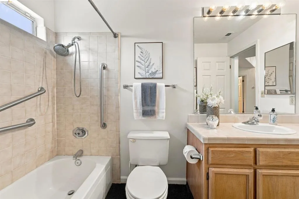 Bathroom featuring a tiled shower/tub combination with grab bars, a single vanity with wood-finish cabinetry, and an integrated basin sink