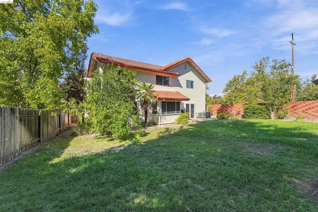 Expansive grassy backyard with a stucco exterior, red tile roof, wood fencing, and mature trees