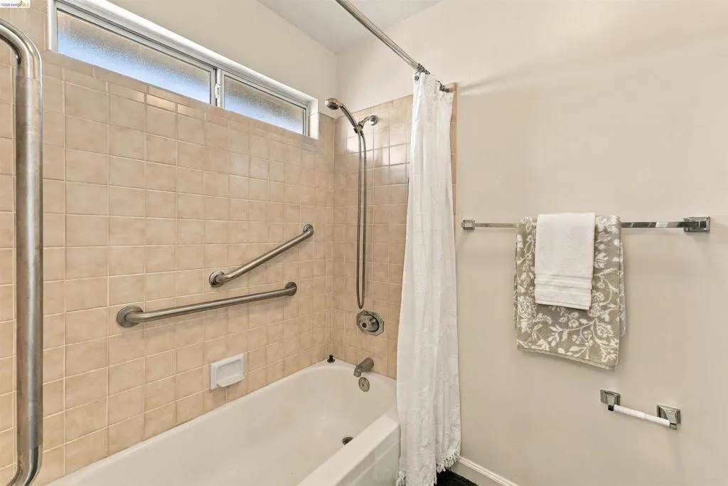 Bathtub with tiled surround, polished chrome fixtures, and high transom window
