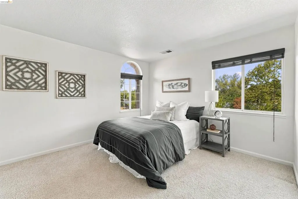 Arched window, rectangular window with dark blinds, light-toned carpeting, and white walls