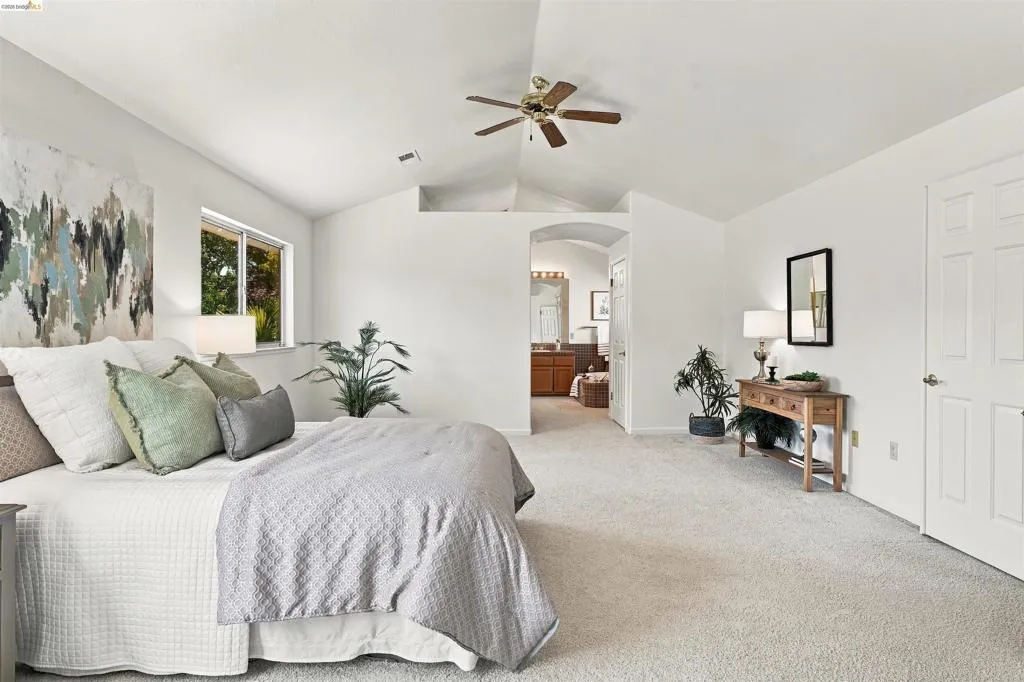Vaulted ceiling with a ceiling fan, carpeted flooring, and a window providing natural illumination