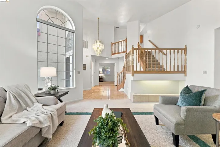 Two-story foyer with an arched, grid-pattern window, wood-finish staircase with balusters, and a tiered chandelier