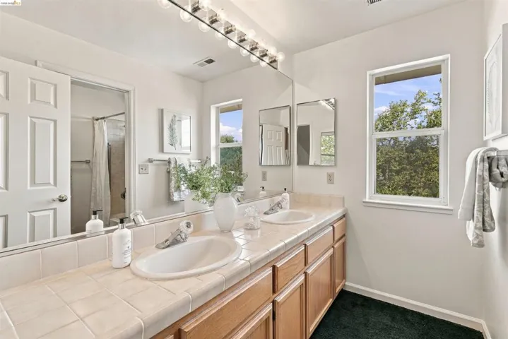 Dual vanity with integrated sinks, tile countertop, and wood-finish cabinetry
