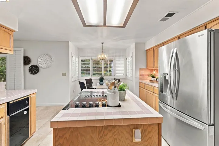 Kitchen featuring stainless steel appliances, wood cabinetry, built-in cooktop, tile flooring, and plantation shutters