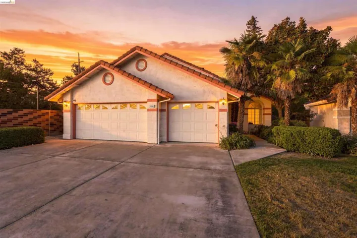 Two-car garage with panel doors, concrete driveway, and stucco exterior with a tile roof