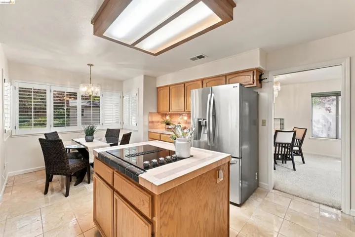 Kitchen featuring a center island cooktop, wood cabinetry, stainless steel refrigerator, and tiled flooring