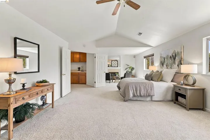 Vaulted ceilings with a ceiling fan, carpeted flooring, two windows, and a built-in wet bar with wood cabinetry
