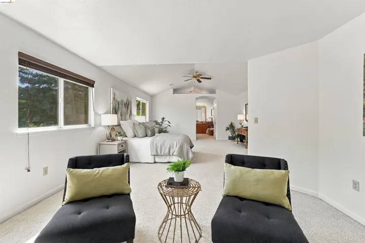 Vaulted ceiling, ceiling fan, white carpet, multiple windows with blinds, and white walls
