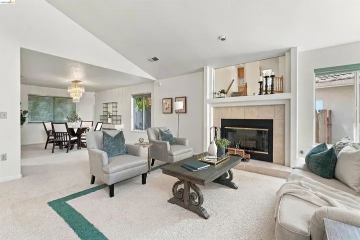 Living area featuring a carpeted floor, tile-surround fireplace, and an open dining area with a tiered chandelier
