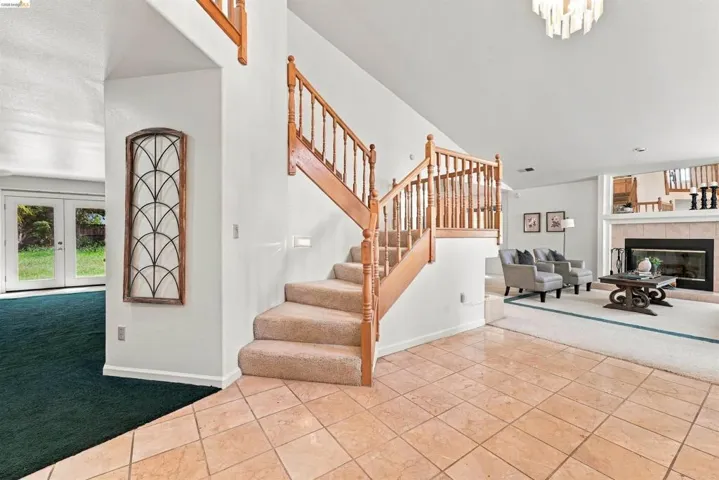 Tile flooring, wood staircase with balusters, fireplace with mantel, French doors, and an overhead light fixture