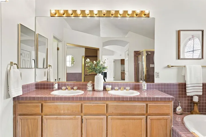 Dual vanity with wood-finish cabinetry, a large wall-mounted mirror, and a tiled countertop
