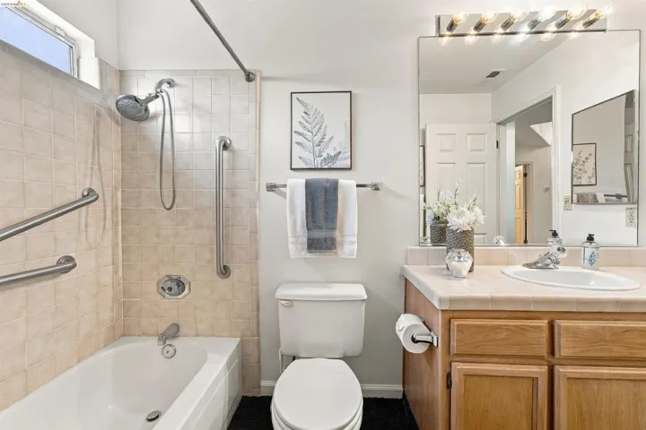 Bathroom featuring a tiled shower/tub combination with grab bars, a single vanity with wood-finish cabinetry, and an integrated basin sink