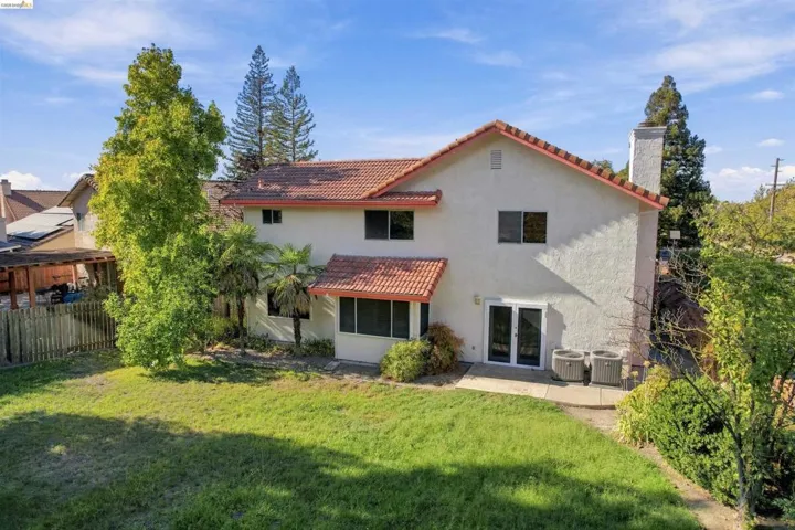 Expansive green lawn with mature trees, stucco exterior, tiled roof, patio access, and a prominent chimney