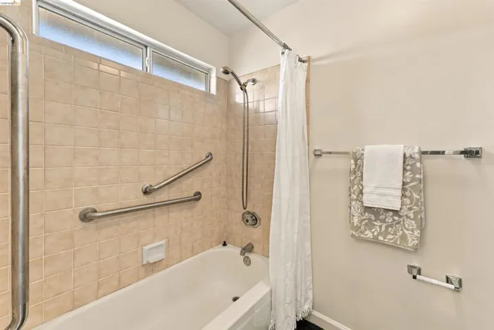 Bathtub with tiled surround, polished chrome fixtures, and high transom window