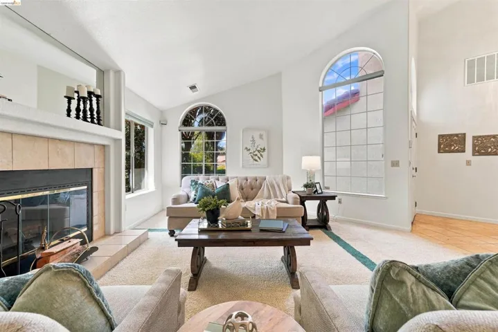 Vaulted ceilings, arched window elements, a tiled fireplace with mantel, and carpet flooring