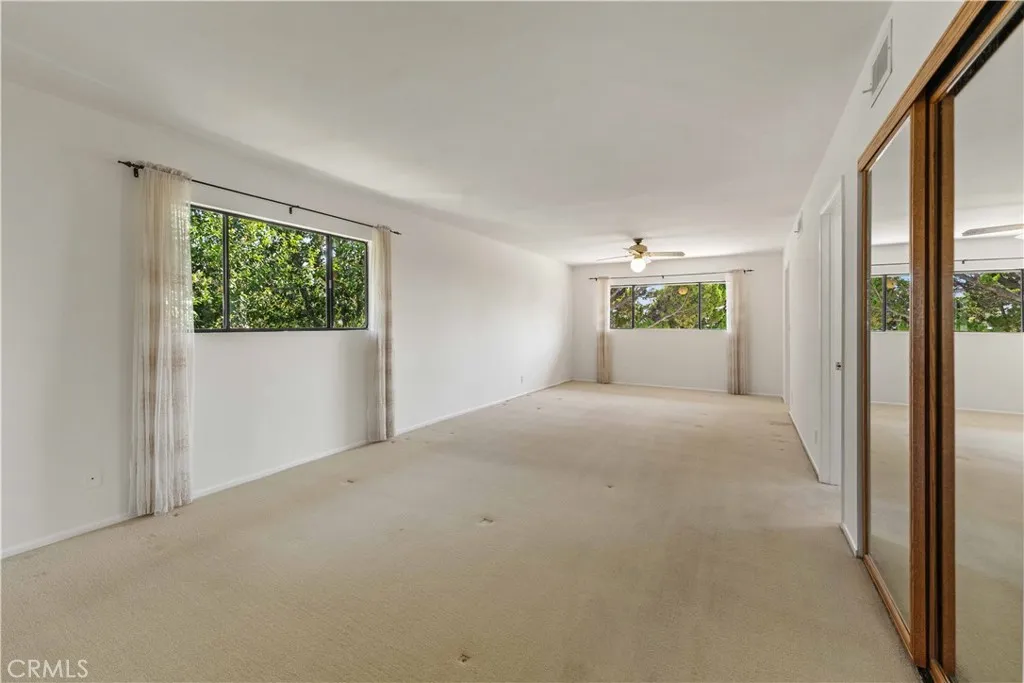 Primary bedroom with room for an office, workout space & views of greenery & a ceiling fan.