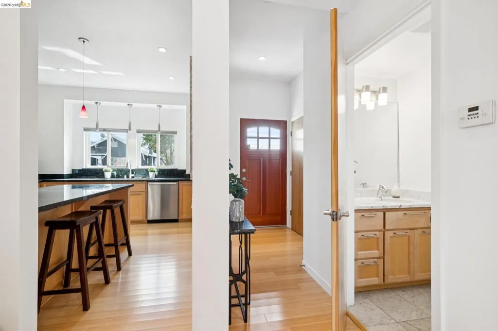 Entry with a paneled wood door and adjacent kitchen featuring a stainless steel dishwasher, black countertops, and pendant lighting Entry with a paneled wood door and adjacent kitchen featuring a stainless steel dishwasher, black countertops, and pendant lighting