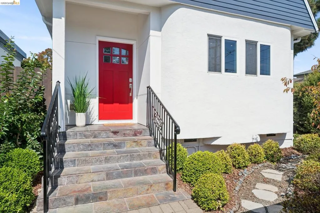 Red paneled entry door with windowpanes, flanked by a white stucco exterior and dark metal handrails Red paneled entry door with windowpanes, flanked by a white stucco exterior and dark metal handrails