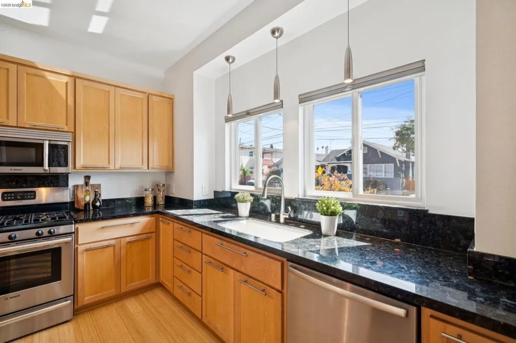 Kitchen featuring light wood cabinetry, dark polished countertops, stainless steel appliances, and two windows Kitchen featuring light wood cabinetry, dark polished countertops, stainless steel appliances, and two windows