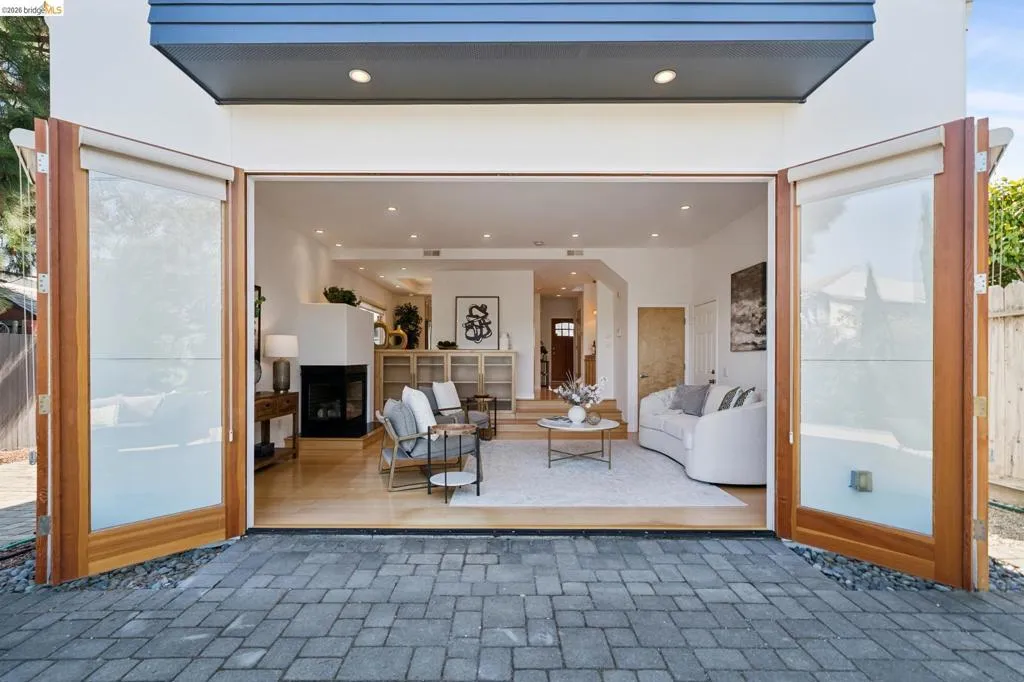 Wide bi-fold glass doors open to a spacious living area with recessed lighting, light wood-finish flooring, and a built-in fireplace Wide bi-fold glass doors open to a spacious living area with recessed lighting, light wood-finish flooring, and a built-in fireplace