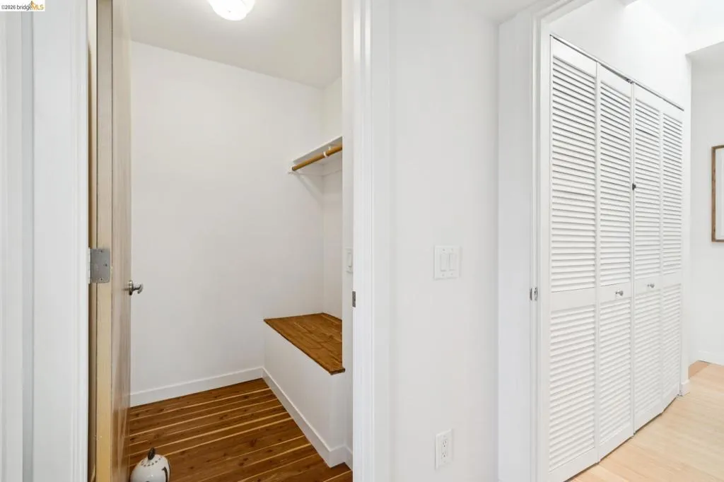 Built-in wooden bench, wood-finish flooring, and white louvered bifold closet doors Built-in wooden bench, wood-finish flooring, and white louvered bifold closet doors