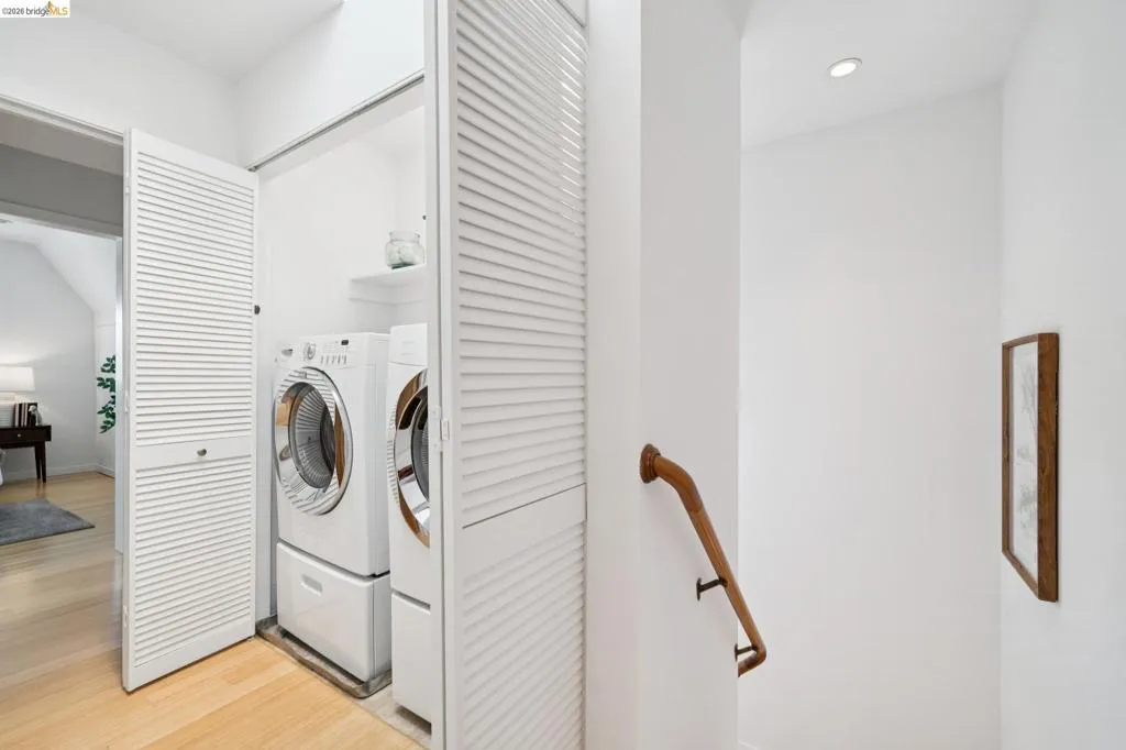 Dedicated laundry closet featuring a stacked washer and dryer, white louvered bifold doors, and overhead shelving Dedicated laundry closet featuring a stacked washer and dryer, white louvered bifold doors, and overhead shelving
