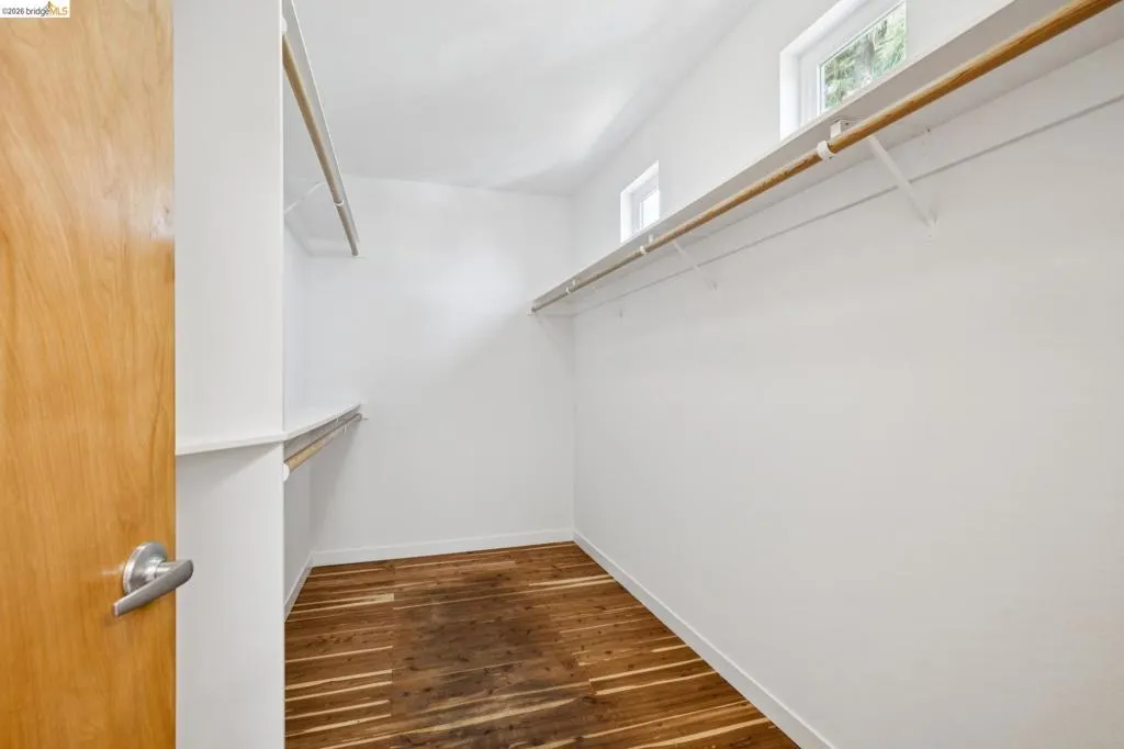 Walk-in closet featuring wood-finish flooring, white walls, and high-set windows Walk-in closet featuring wood-finish flooring, white walls, and high-set windows