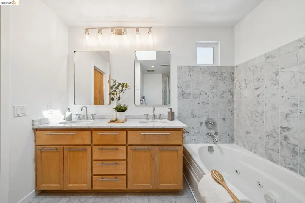 Double vanity with wood-finish cabinetry, dual rectangular mirrors, and a full-size bathtub with a tiled surround Double vanity with wood-finish cabinetry, dual rectangular mirrors, and a full-size bathtub with a tiled surround