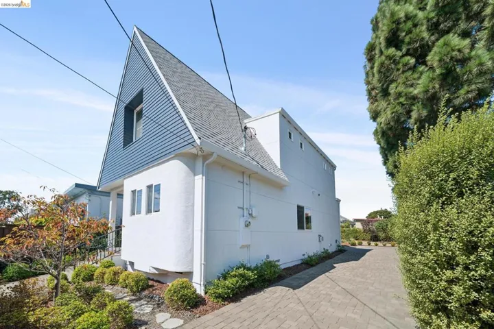 Exterior featuring a prominent peaked roof with shingle siding, a white stucco facade, and a paved driveway