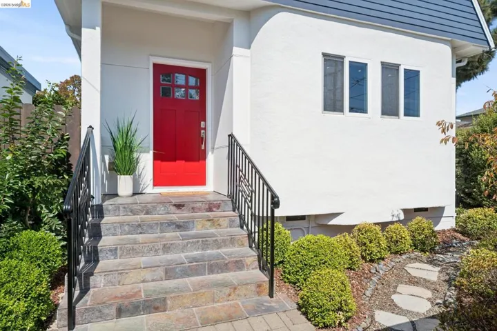 Red paneled entry door with windowpanes, flanked by a white stucco exterior and dark metal handrails