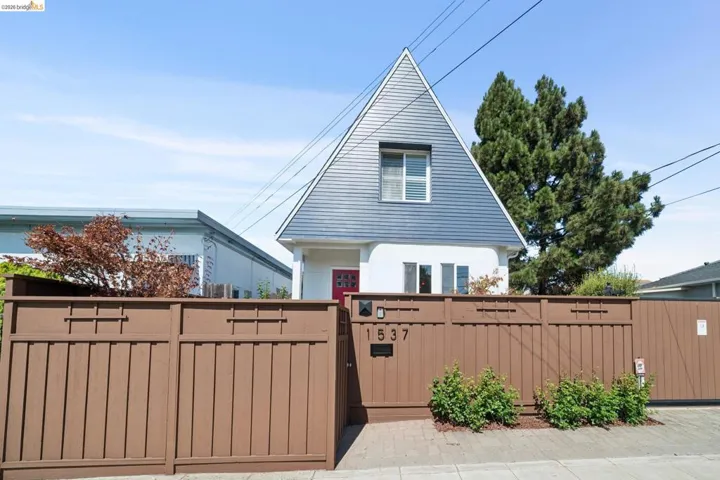 Distinctive architectural exterior featuring a steeply pitched roof with siding, a red entry door, and a private wooden fence
