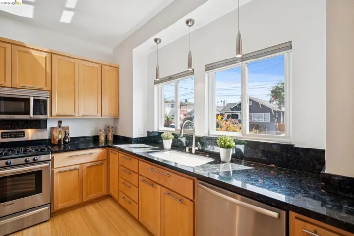Kitchen featuring light wood cabinetry, dark polished countertops, stainless steel appliances, and two windows