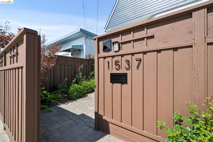 Entry gate with applied numbers and integrated mailbox, paver walkway, and lush landscaping