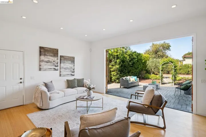 Recessed lighting, wood-finish flooring, and a folding glass wall open to a paver patio with a garden archway